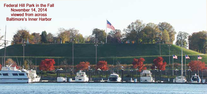 Image of Federal Hill Park in November viewed fron across the harbor with U.S. flags flying, colorful fall foliage &amp; yachts in the foreground, Baltimore, MD