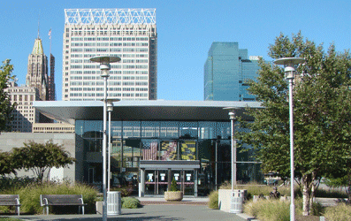 Entrance to the Baltimore Visitor Center with 1814 Replica US Flag, Maryland Flag, and Baltimore Flag hanging above the doors with Baltimore skyline in background, West Shore Park, Inner Harbor