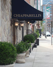Attractive sidewalk view of the deep blue awning & old world lanterns at the welcoming entrance to Chiapparelli's Italian Restaurant with georgeous planters filled with lush green plants lining the way on High Street in the heart of Little Italy and green red & white street banners of the Italian peninsula in the background, Baltimore, MD