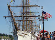 Image of visiting tall ship with colorful pennants flying in the mast docked at the Inner Harbor Promenade including a U.S. flag on the lamppost in the foreground for the Star-Spangled Sailabration in June 2012 Baltimore, MD