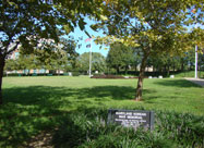 Image of Maryland Korean War Memorial with plackard commemorating those who served in the foreground with flags flying in the background, located at Canton Waterfront Park on Boston Street in Baltimore, MD